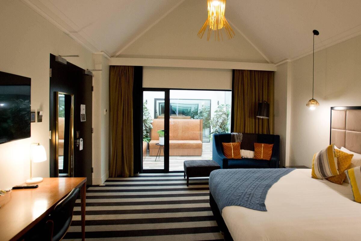 A hotel room with a bed, a desk, a television, a chair, and a view of the outdoors.