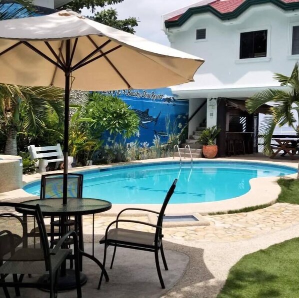 A swimming pool with a mural, outdoor seating, and a white building in the background. - Love S Beach And Dive Resort (Moalboal)