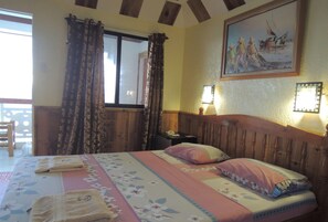A bedroom with a wooden headboard, a bed with floral bedding, a window with curtains, a painting on the wall, and a nightstand with a lamp. - Love S Beach And Dive Resort (Moalboal)