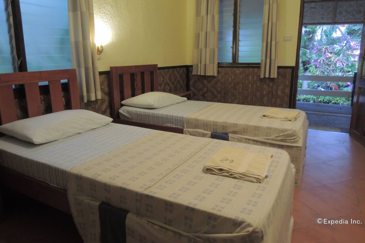 A room with two single beds, each with a pillow and a neatly folded towel.