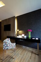 A reception desk with a flat-screen TV, a desk lamp, a vase with pink flowers, and a chair with a colorful pattern.