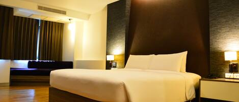 Una habitación de hotel con una cama grande, una mesita de noche con lámpara, un respiradero en la pared y una ventana con cortinas.