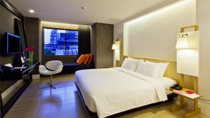 A hotel room with a large bed, a desk with a chair, a TV, and a window with a view of buildings.