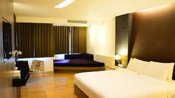 Habitación de hotel con una cama grande, un sofá, una silla, un televisor y una ventana con cortinas.