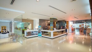 A modern hotel lobby with glass partitions, a reception desk, and a visible restaurant area.