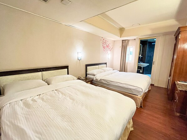 Une chambre d’hôtel avec deux lits, une table de chevet avec une lampe, une salle de bain avec un lavabo et une porte donnant sur une autre pièce.