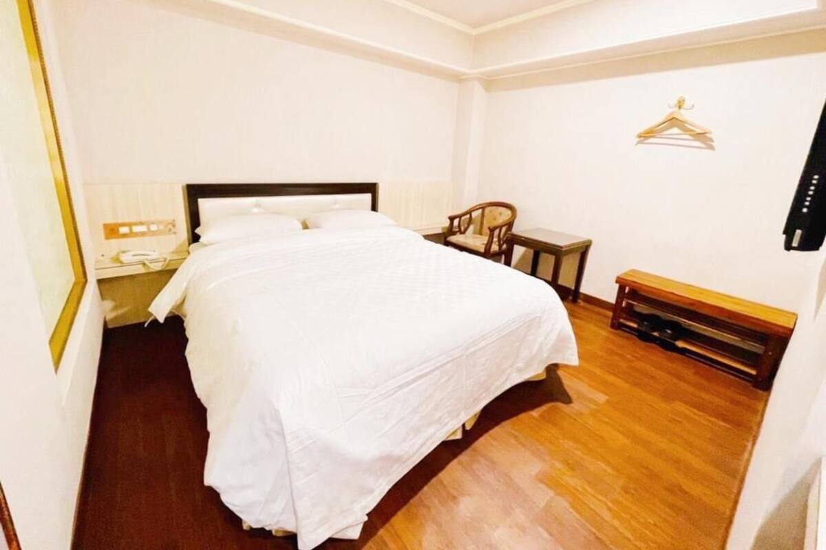 Una habitación de hotel con una cama grande, una mesita de noche, una silla y un banco de madera.
