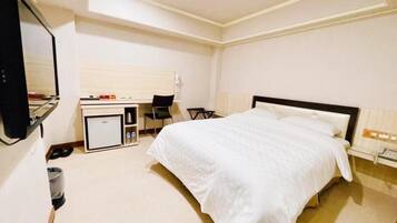 A hotel room with a bed, a desk, a chair, and a small kitchenette.