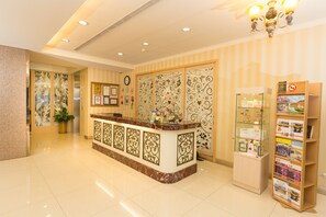 Un espace d’accueil d’hôtel avec un comptoir en marbre, un élément de séparation décoratif, une horloge et un présentoir pour les brochures.