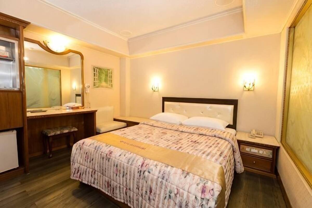 Una habitación de hotel con cama, mesita de noche, escritorio, silla y espejo.