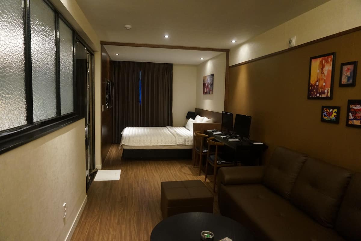A hotel room with a bed, a desk with a chair, a sofa, and a TV.