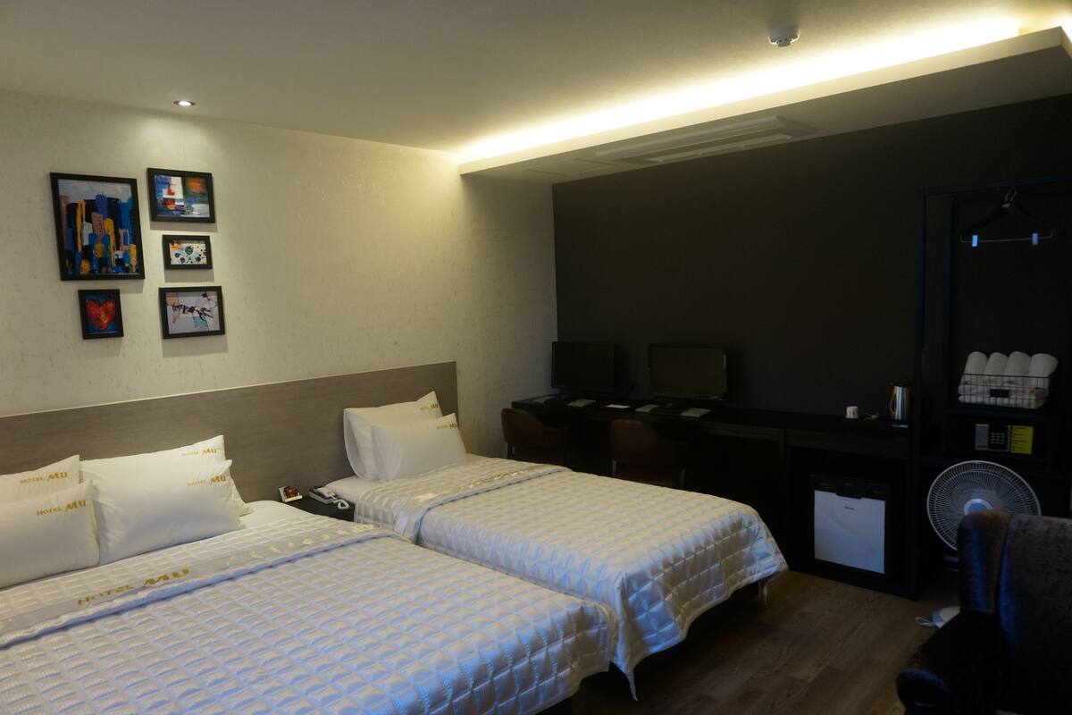A hotel room with two beds, a desk, a chair, and a TV.