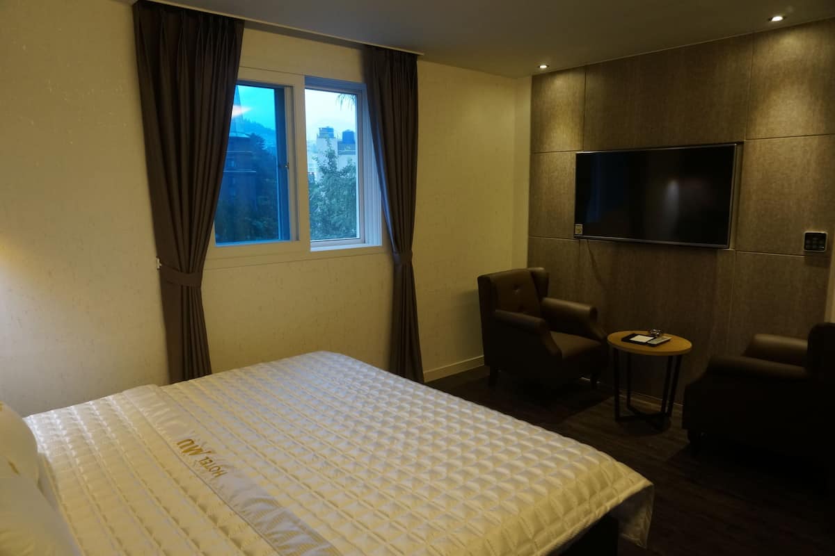A hotel room with a bed, a TV mounted on the wall, a small table, and two chairs.
