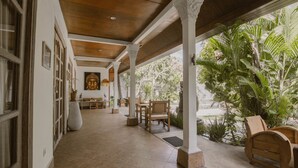 Un espacio exterior cubierto con mobiliario de madera, piso de baldosas y vista a la vegetación.