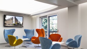 Un intérieur moderne avec une grande fenêtre, plusieurs chaises et un téléviseur à écran plat fixé au mur.