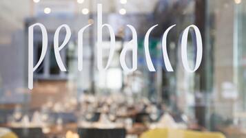 Vista borrosa del interior de un restaurante o cafetería, con la palabra 'perbacco' destacada en una ventana de vidrio.