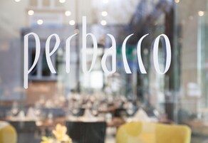Vista borrosa del interior de un restaurante o cafetería, con la palabra 'perbacco' destacada en una ventana de vidrio.