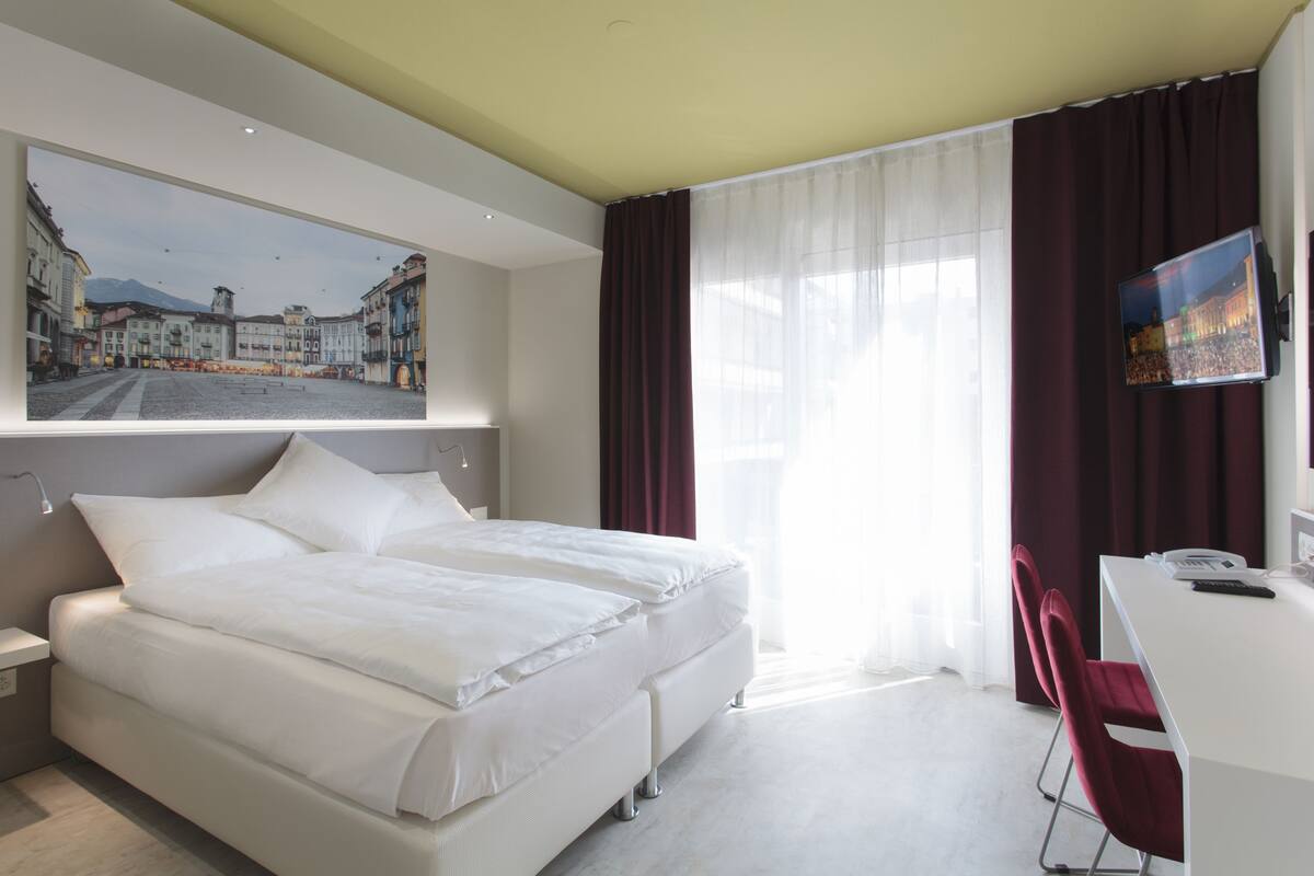 A modern hotel room with a large bed, a desk, and a television.