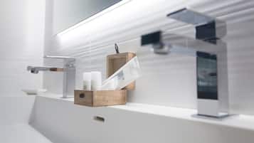 Ein modernes Badezimmer mit klarem, minimalistischem Design, das ein weißes Waschbecken, eine Holz-Seifenschale und eine Glasdusche zeigt.