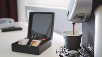 Máquina de café servindo café em uma xícara, com uma caixa de cápsulas de café e um smartphone sobre a mesa.