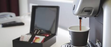 A coffee machine dispensing coffee into a cup, with a box of coffee pods and a smartphone on a table.