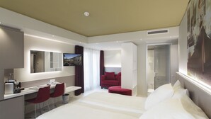 Une chambre d’hôtel moderne dotée d’un grand lit, d’un bureau avec deux chaises, d’une télévision et d’un espace douche.