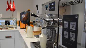 A coffee machine with a Nespresso label, a milk frother, and a glass of milk on a counter.