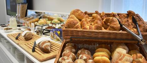 Un bufé con diversos panes y pasteles, incluyendo croissants y barras, exhibidos en tablas de madera y cestas de mimbre.