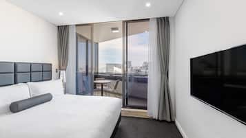 Habitación de hotel con una cama grande, un televisor de pantalla plana, un balcón con mesa y sillas, y vistas a la ciudad.