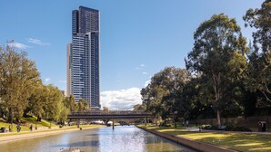 Un río con un puente, un edificio alto identificado como 'Meriton', y un parque con árboles y césped.
