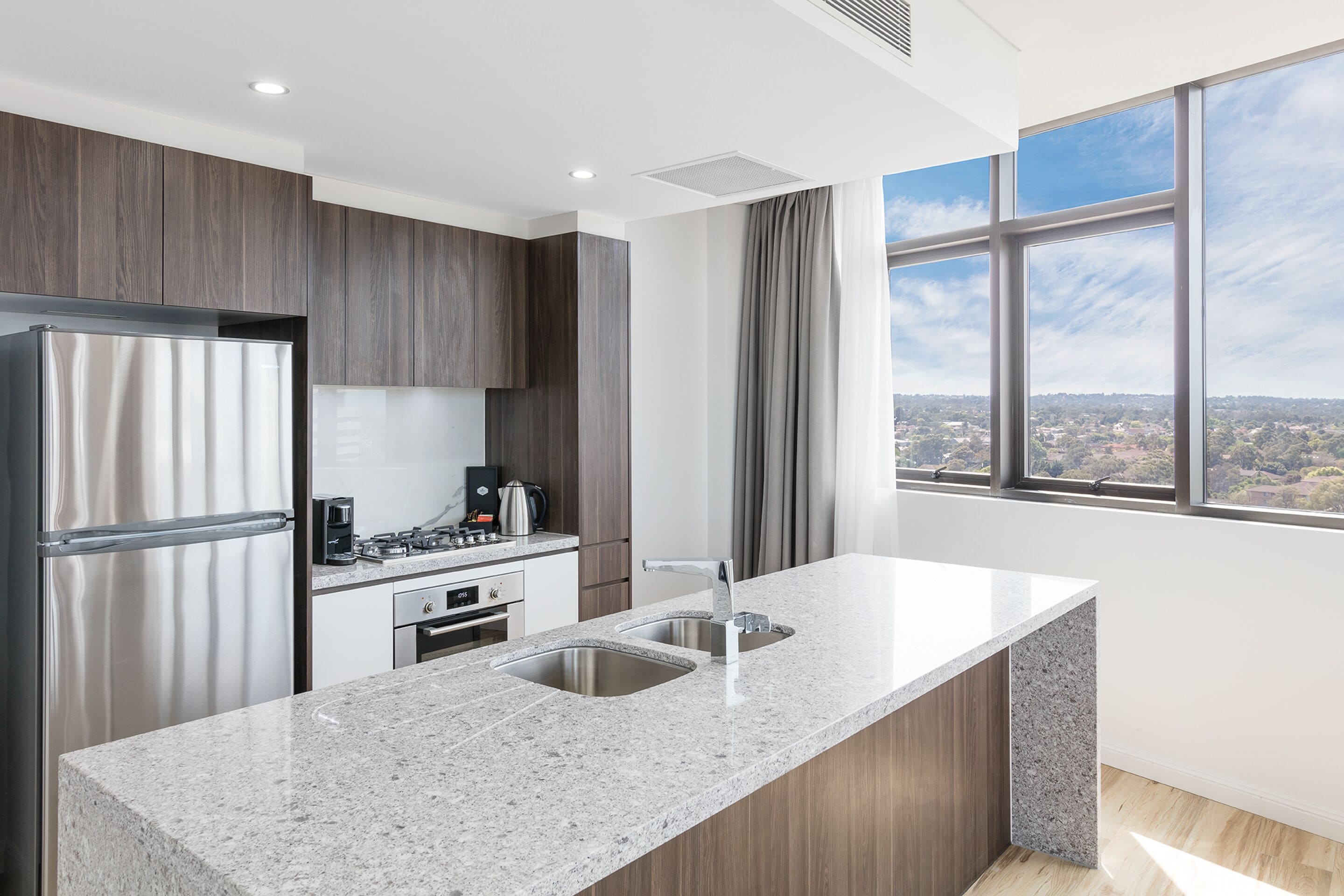 A modern kitchen with a granite countertop, stainless steel appliances, and a large window offering a city view.