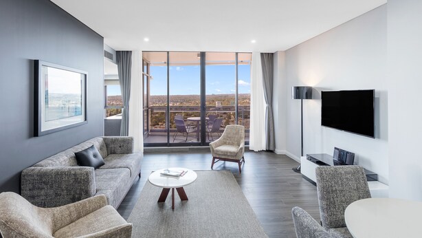 Uma sala de estar moderna com sofá, poltronas, mesa de centro, televisão e varanda com vista para a cidade.