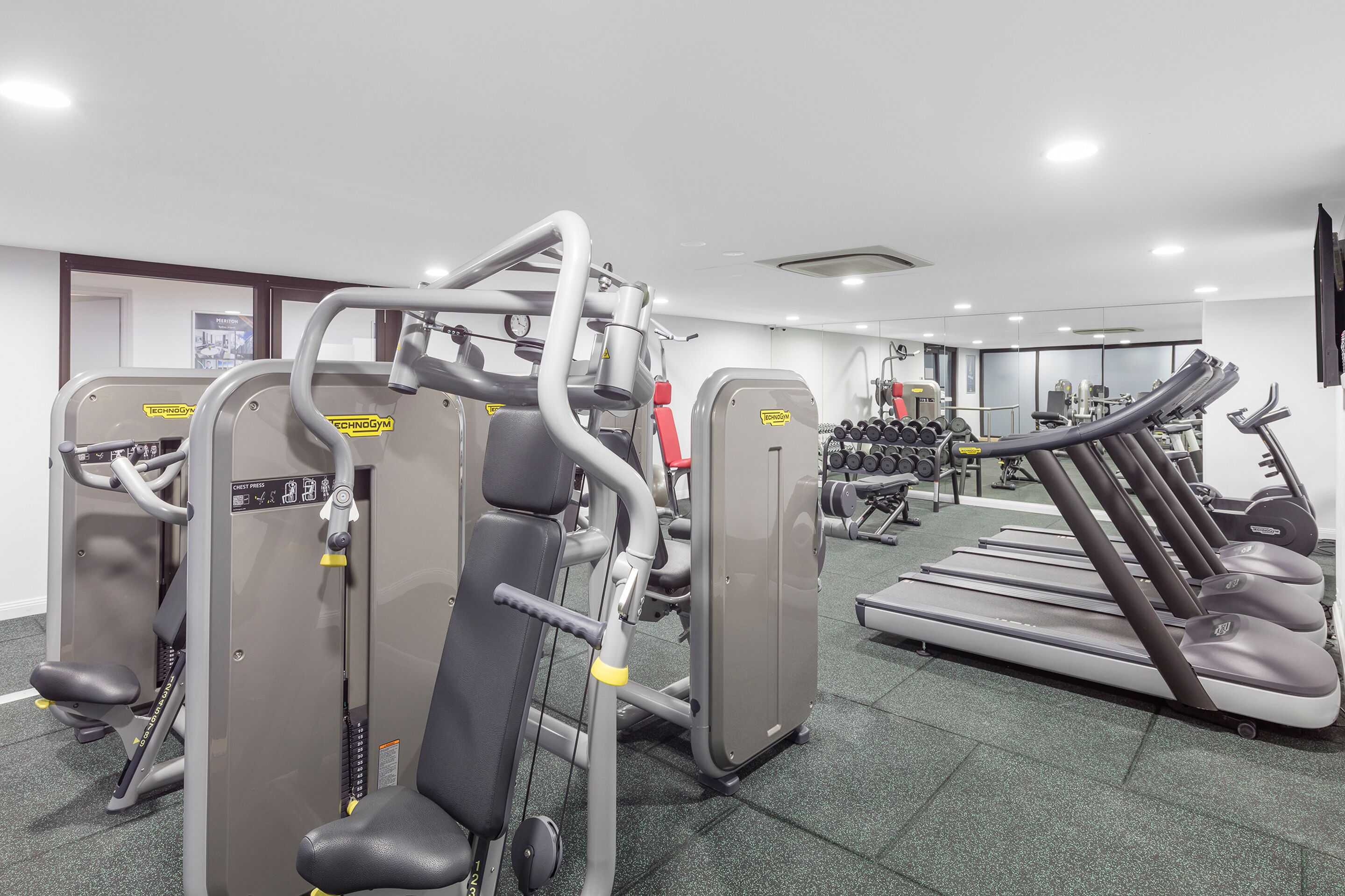 Een sportschool met cardioapparatuur, gewichthefmaterialen en een spiegelwand.