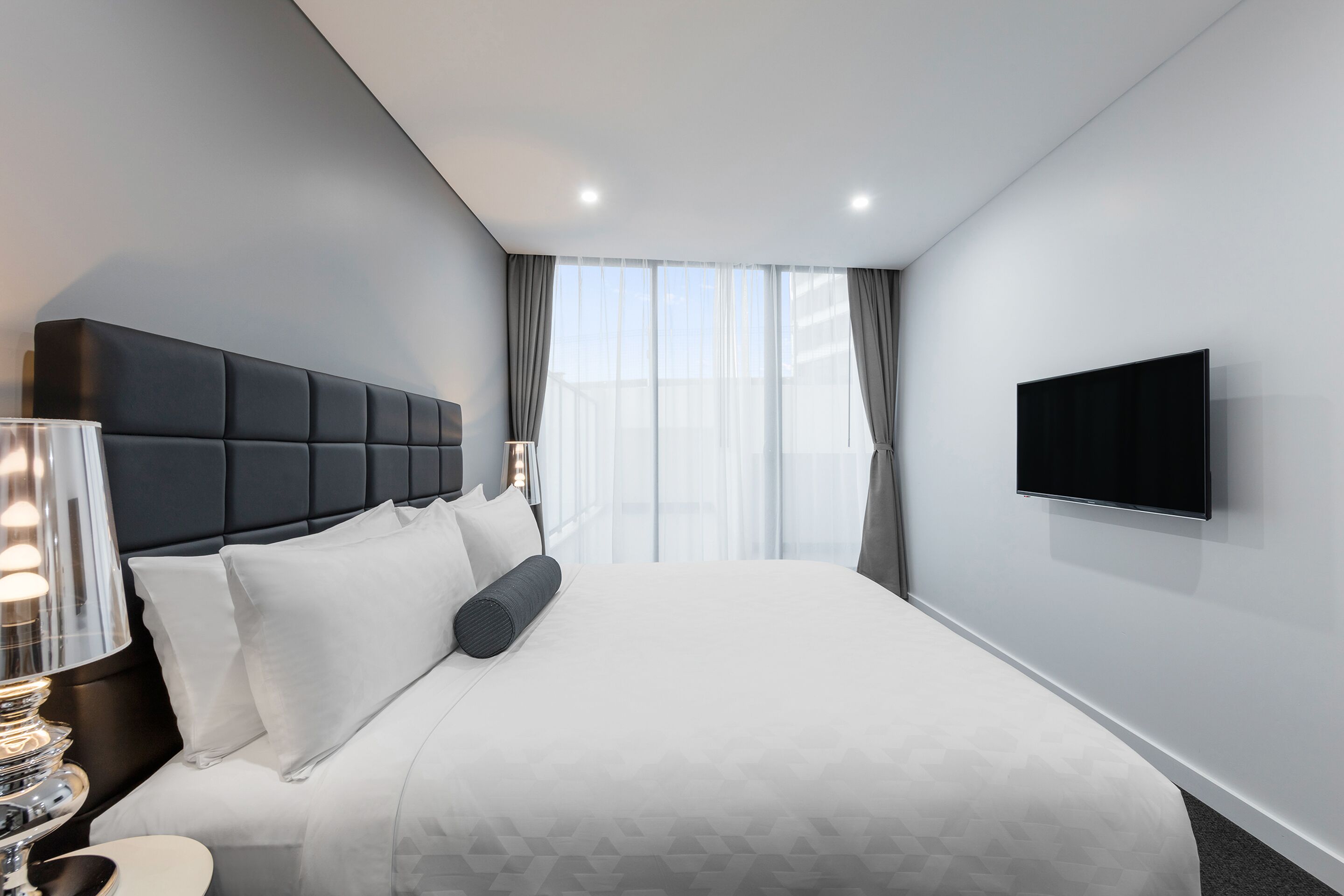 A modern hotel room with a large bed, a flat-screen TV, and a window with curtains.