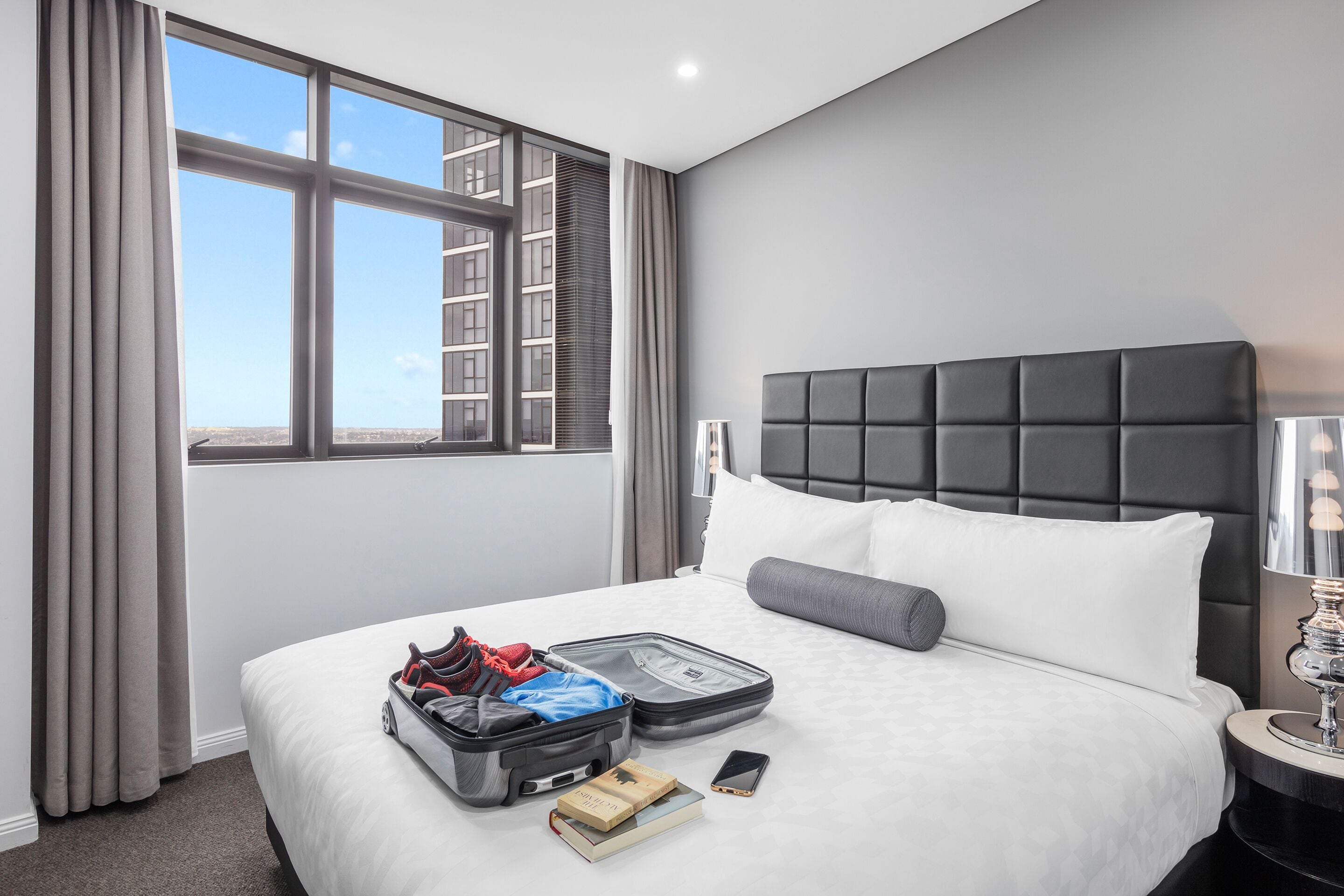 Une chambre d’hôtel avec un grand lit, une valise, un livre et une lampe.