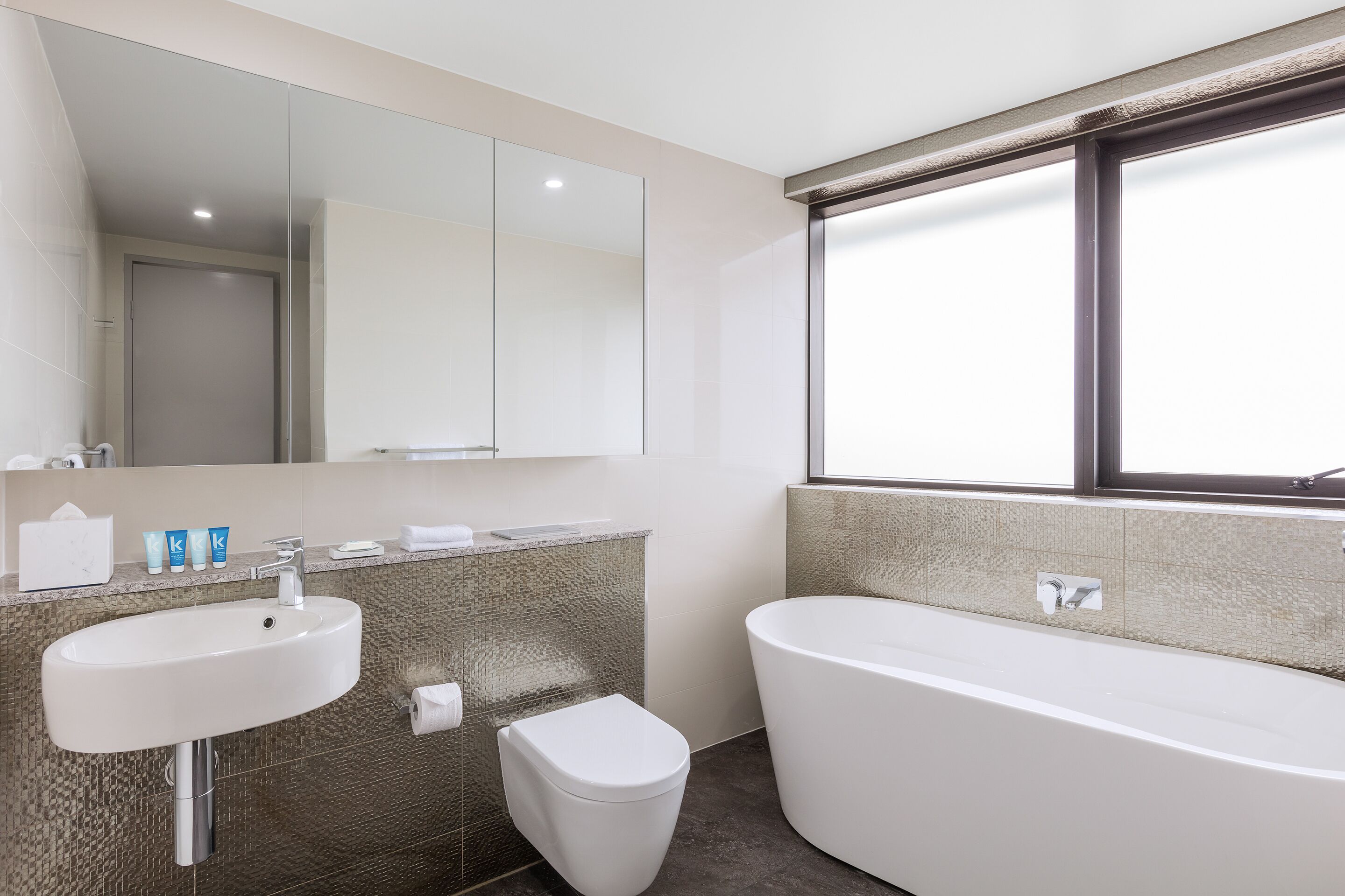 Een moderne badkamer met een groot wit wastafelmeubel, toilet en bad.