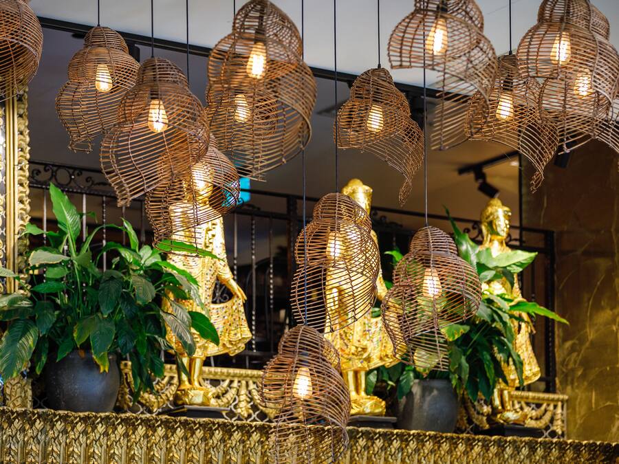 A room with ornate golden decorations, a large potted plant, and hanging wicker light fixtures.