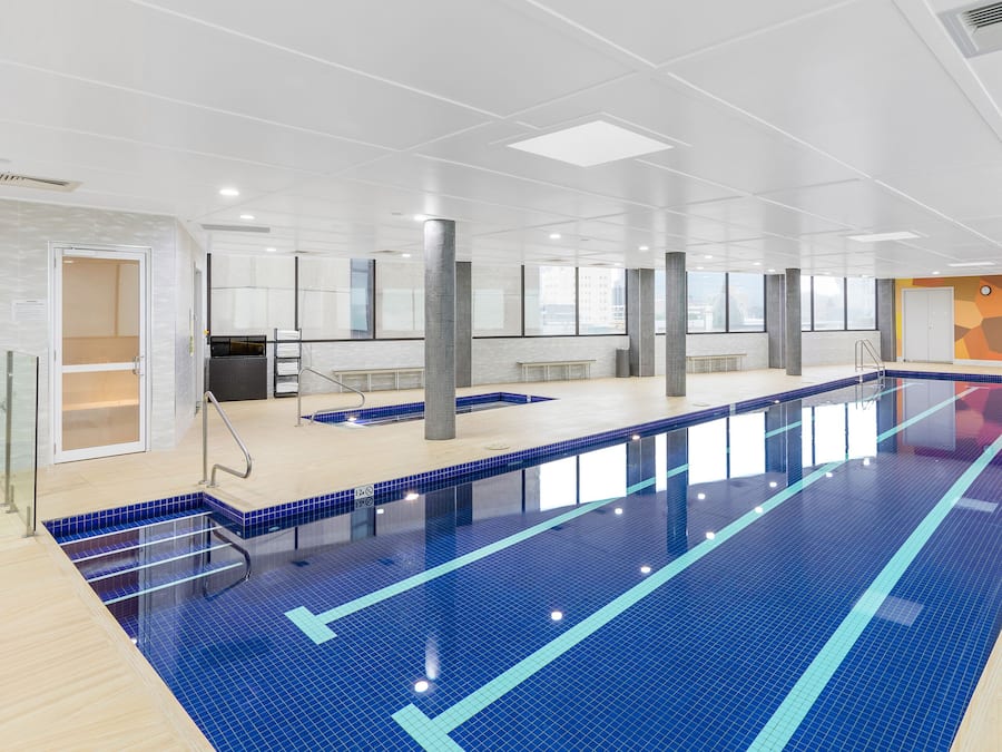Une grande piscine intérieure avec des couloirs bien délimités, une zone de pont en bois et un design de plafond moderne.
