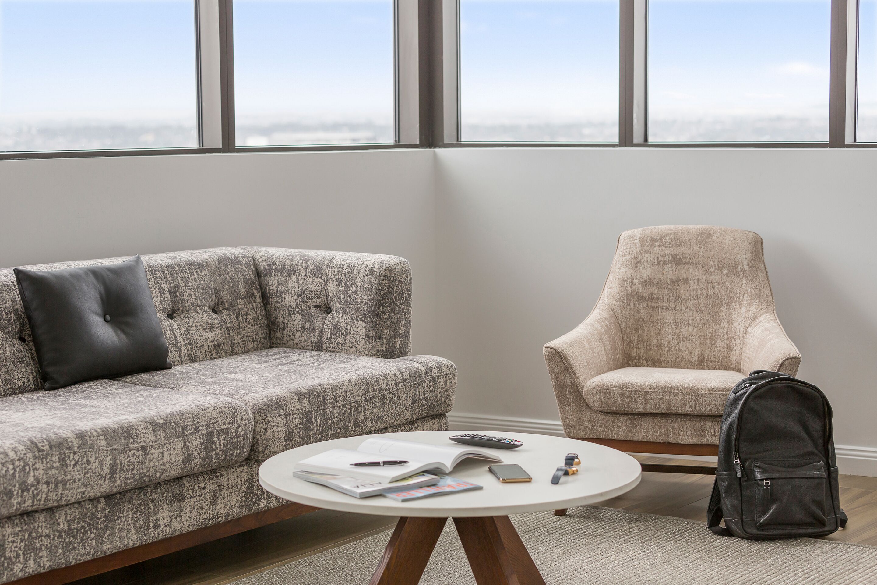 Una sala de estar moderna con un sofá gris, un sillón beige y una mesa de centro redonda con libros y un control remoto.