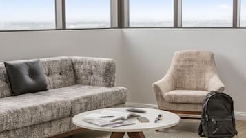 Un salon moderne avec un canapé gris, un fauteuil beige et une table basse ronde sur laquelle sont posés des livres et une télécommande.