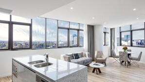 Um apartamento moderno com cozinha, sala de estar e área de jantar. Possui janelas amplas, vista para a cidade e mobiliário contemporâneo.