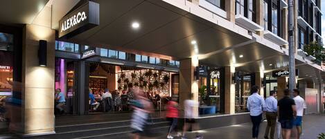 A modern building with a prominent 'ALEX&CO.' sign, featuring a glass storefront and outdoor seating area.