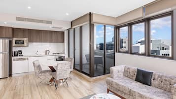 A modern apartment with a kitchen, dining area, and living room. It features a large sliding glass door to a balcony, a sofa, and a coffee table.