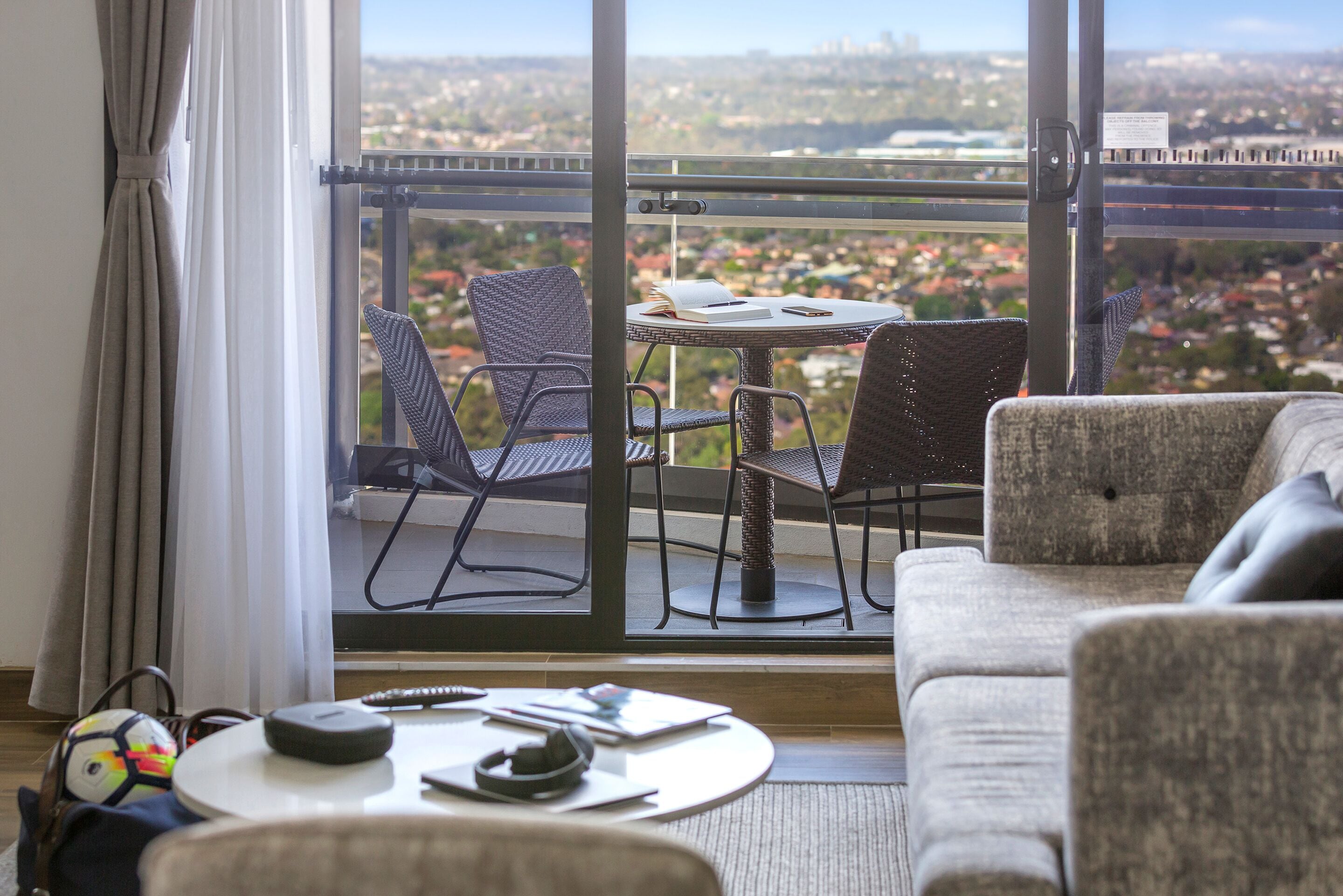 Un balcón con sillas de mimbre y una mesa, con vistas a un paisaje urbano.