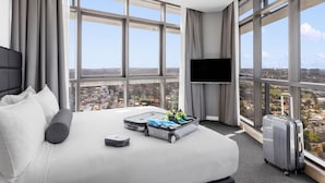 Quarto de hotel com uma cama grande, televisão e vista para o horizonte urbano através de amplas janelas.
