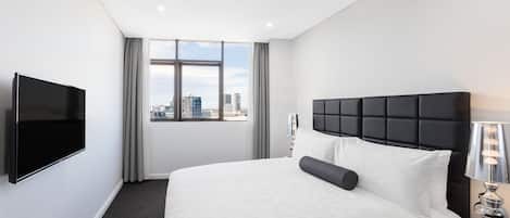 Habitación de hotel con una cama grande, un televisor de pantalla plana, una ventana con vista a la ciudad y una mesita de noche con una lámpara.