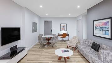 Uma sala de estar moderna com televisão de tela plana, sofá, mesa de centro e um espaço de jantar com cadeiras e uma mesa.