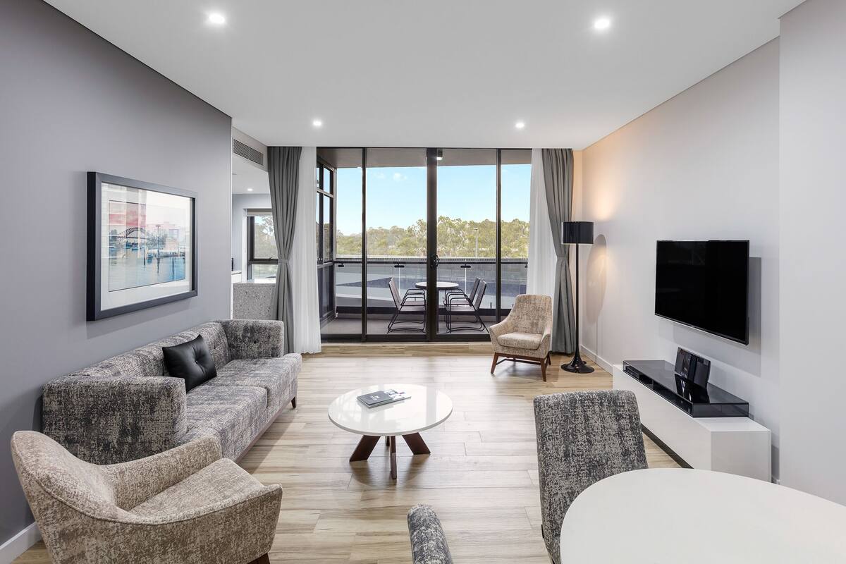 Ein modernes Wohnzimmer mit einer Couch, Sesseln, einem Couchtisch, einem Fernseher und einem Balkon mit Blick.