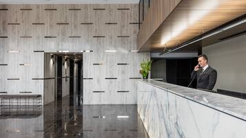 Een moderne hotel lobby met een marmeren receptiebalie, een bank en een plant.