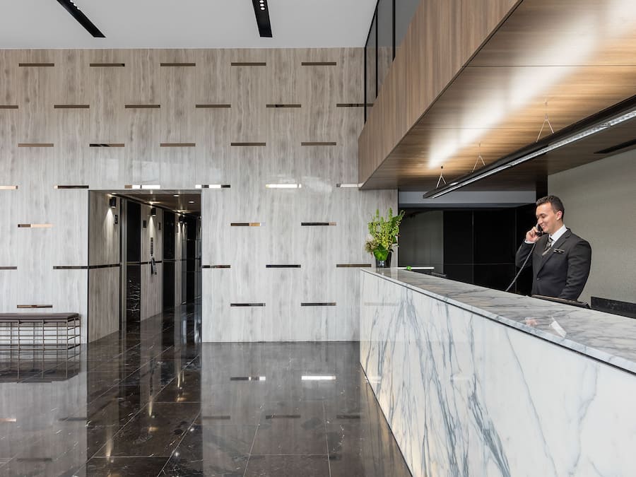 Een moderne hotel lobby met een marmeren receptiebalie, een bank en een plant.